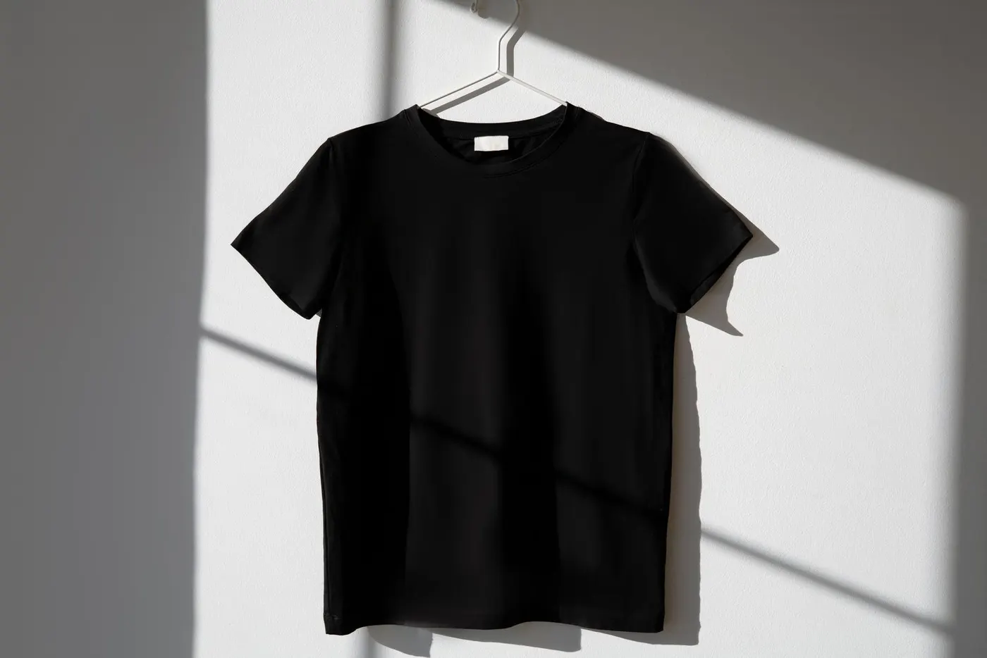 A black T-shirt on a hanger against a white wall